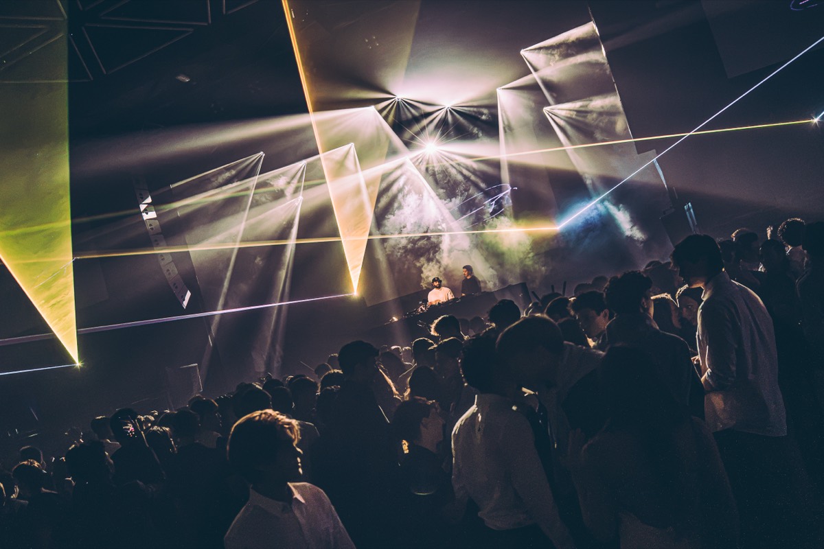 Two DJs on stage framed by white laser planes