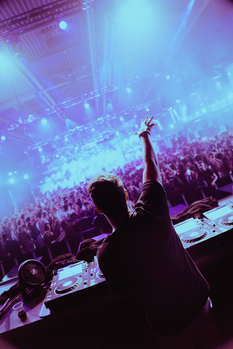 DJ with arm raised facing the Ascension crowd from behind the decks