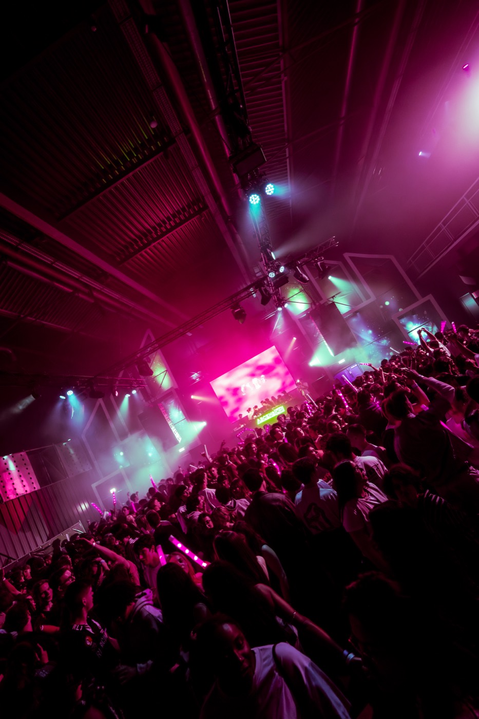 Packed Ascension hall under pink and green stage lighting, glow sticks raised