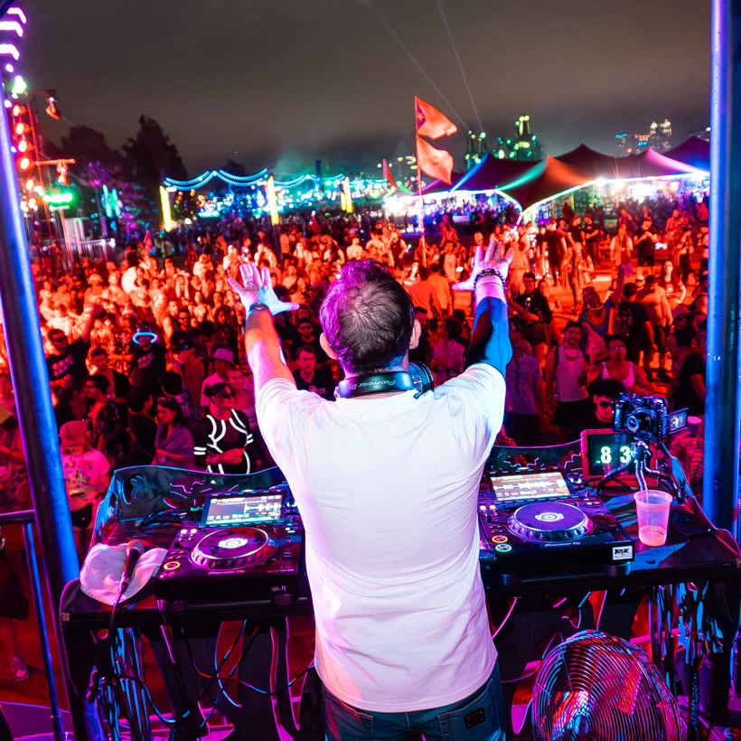 Tim Clark behind the decks with both arms raised to a festival crowd at night